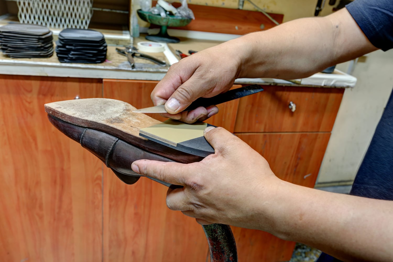 Le mani del calzolaio applicano una nuova suola a una scarpa tenuta sulla forma