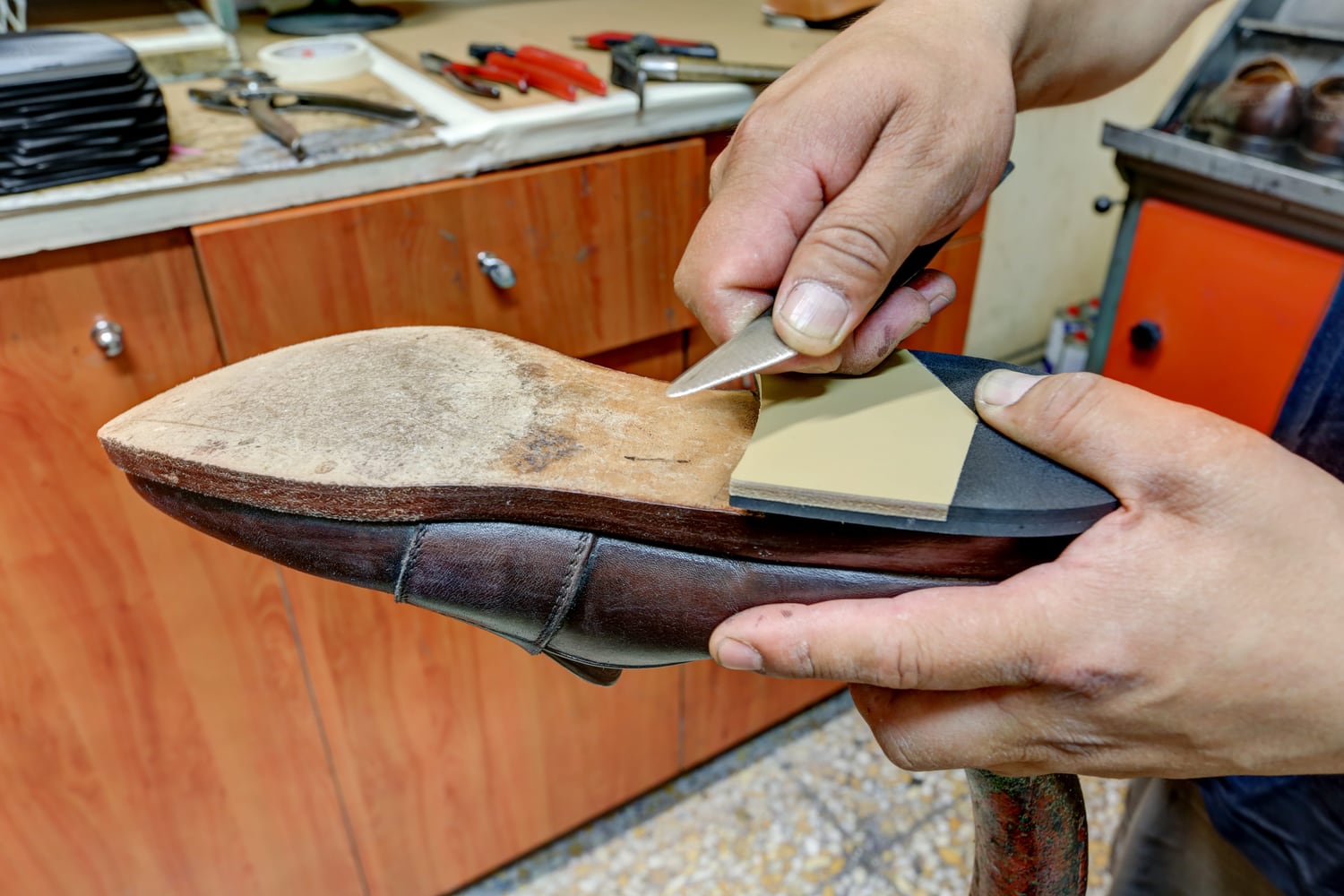 Le mani del calzolaio rifilano con la trincetta il bordo di una suola