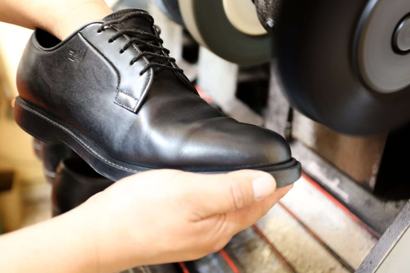 Una scarpa da uomo rifinita, tenuta in mano accanto alla lucidatrice